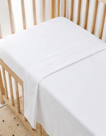 Sábana bajera y encimera Cotton Bio de algodón orgánico colocadas y bien ceñidas en una cuna de madera natural